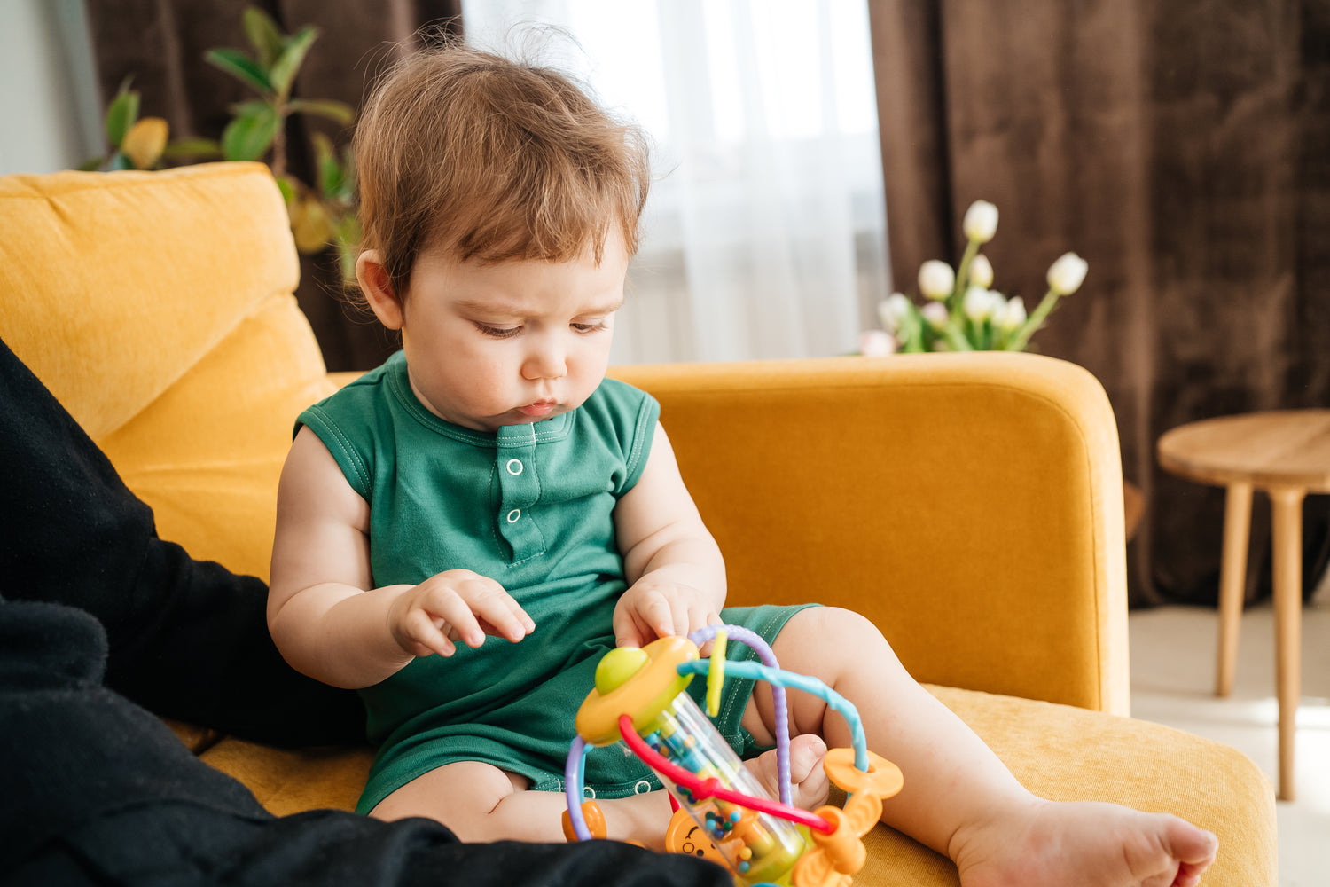 Young dad plays with his baby son on a yellow sofa
